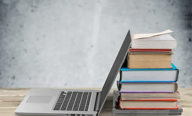 Open laptop up against a stack of books